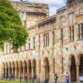 The sandstone buildings of UQ's Great Court with people wandering in the background.